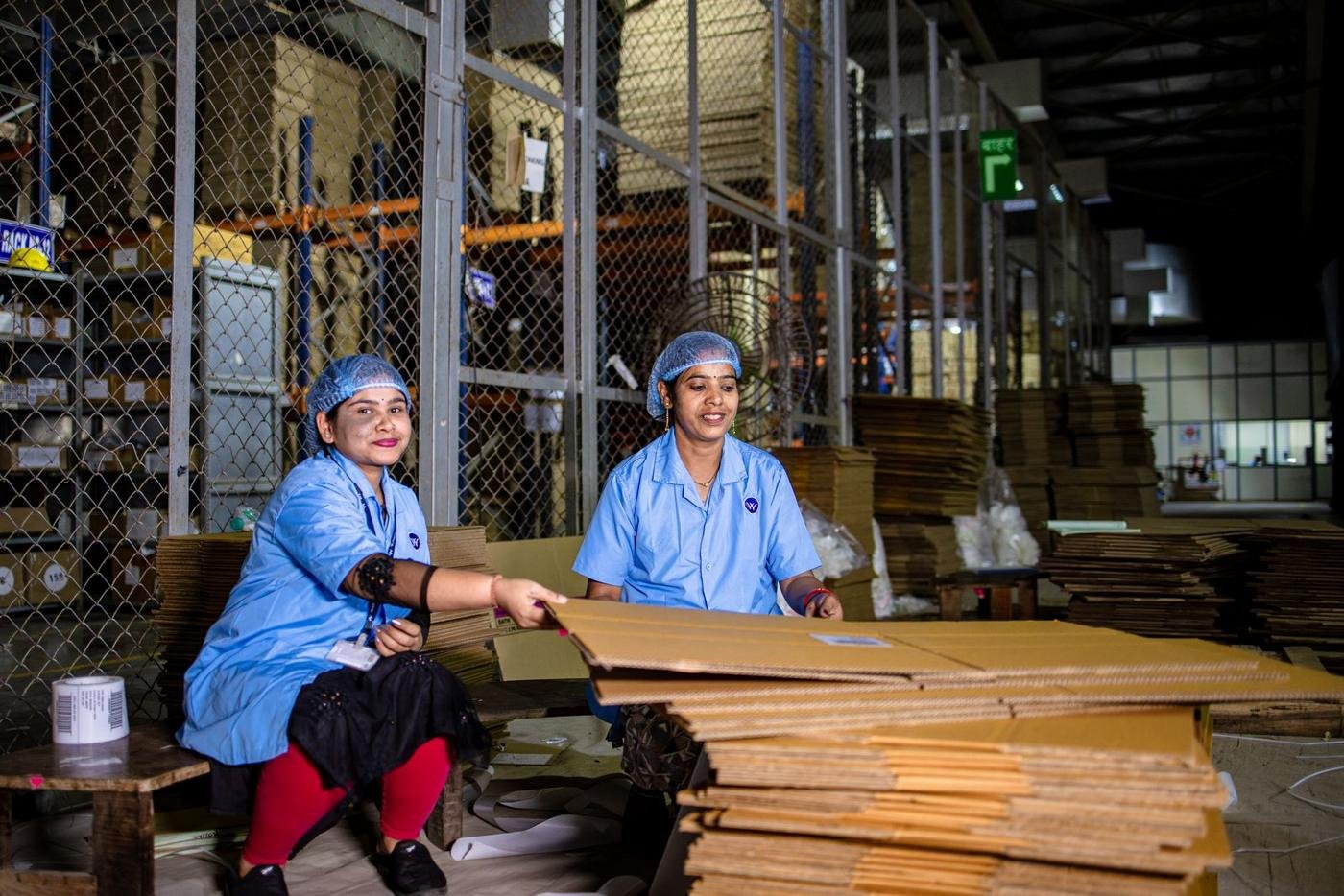 Two women handling cardboard boxes at a warehouse in India